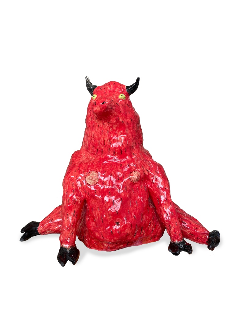 A photograph of a ceramic sculpture of a fat red demon with black horns and black cloven hooves sitting with it's legs sticking out to the sides.